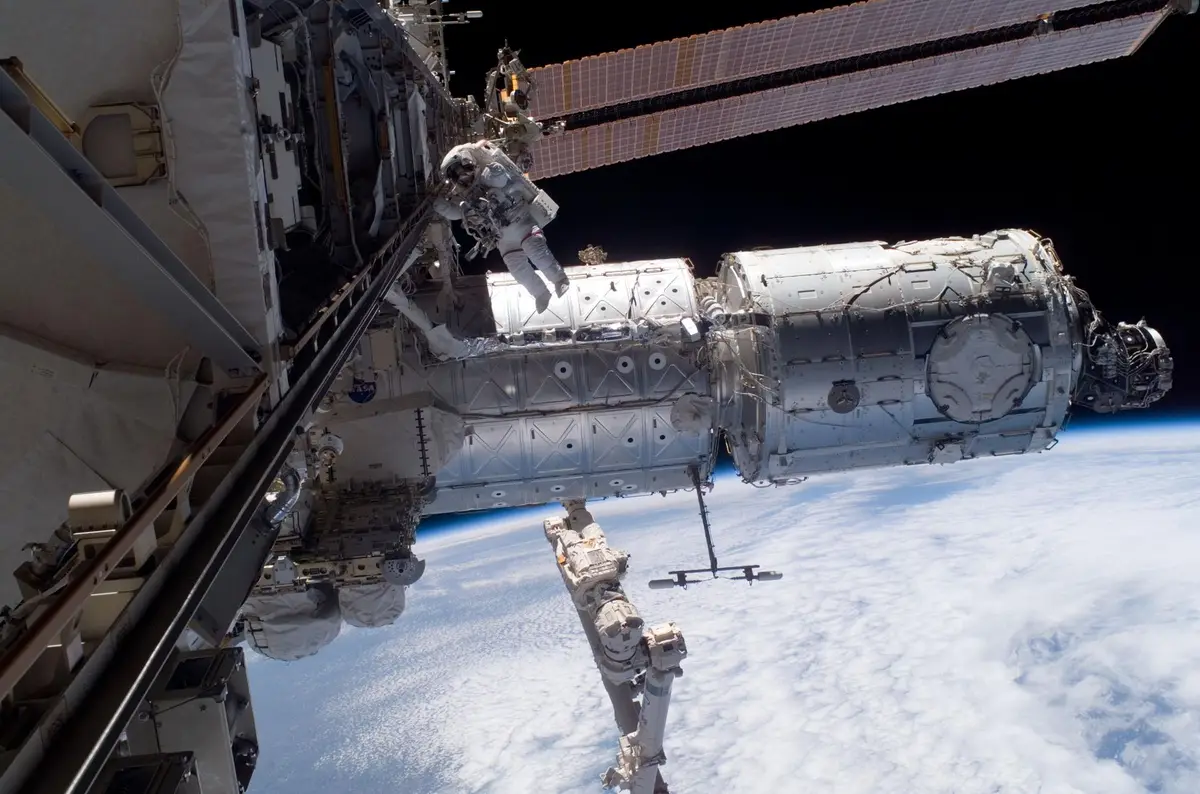 Astronaut in a spacesuit working on the outside of the International Space Station, with Earth's curved horizon and white clouds below