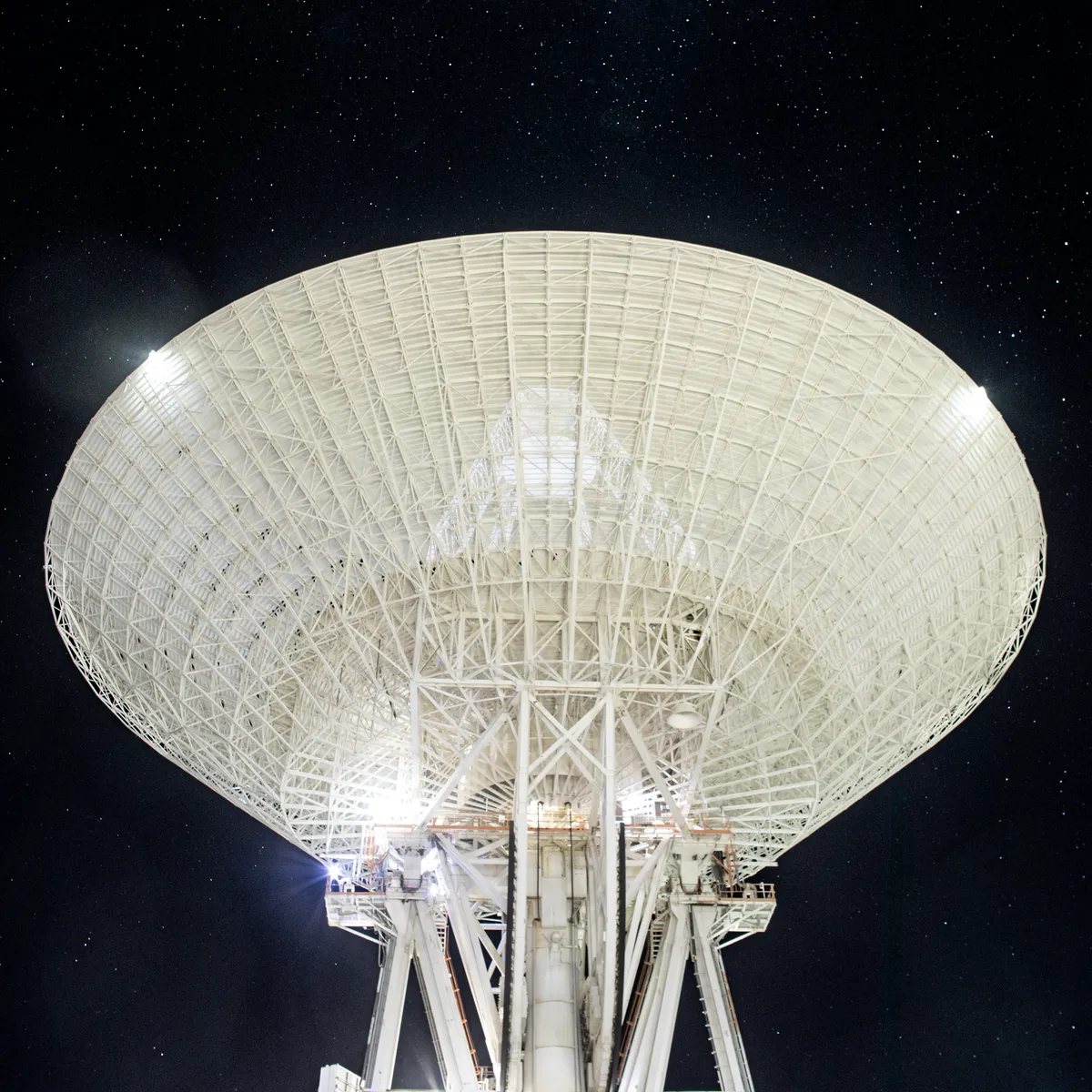 A giant white radio dish antenna pointing up at a sky full of stars at night