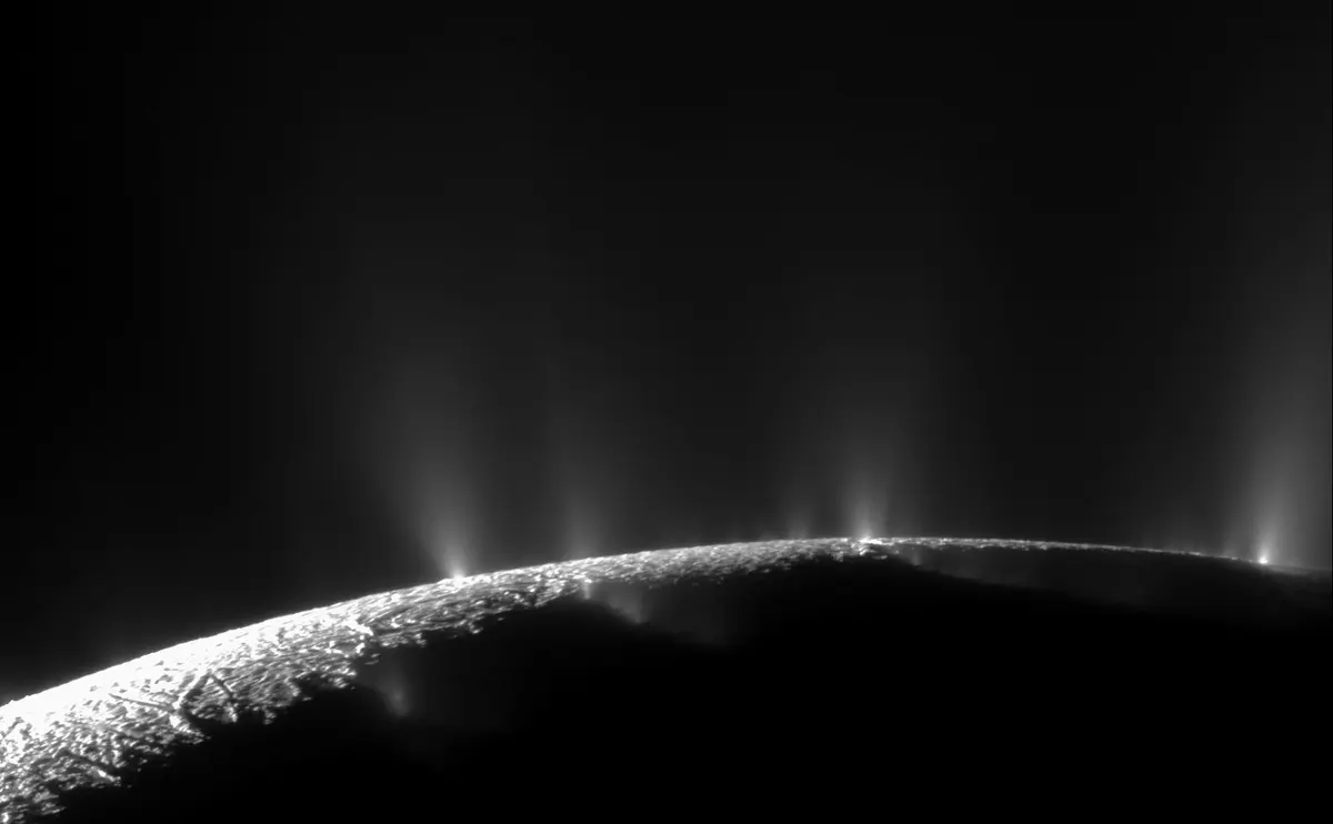The bright icy edge of Enceladus against black space, with thin jets of water ice spraying upward from the south polar region