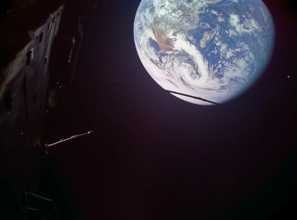 Photo from Juice's monitoring camera showing Earth in the upper right with Africa and Madagascar under swirling clouds, and part of the spacecraft's boom and structure in the dark foreground