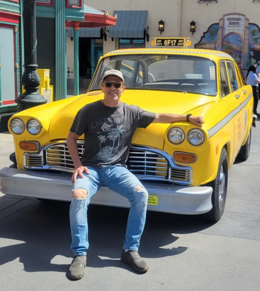 Marcos Salles sitting on the bumper of a yellow checker taxi at Universal Studios