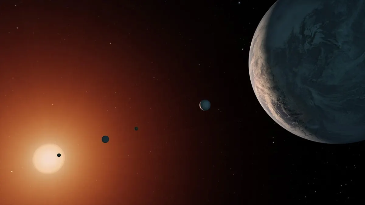 Artist's concept of the TRAPPIST-1 system: a glowing red-orange star at left with a small dark planet crossing its face, more planets in a line, and a large planet at right