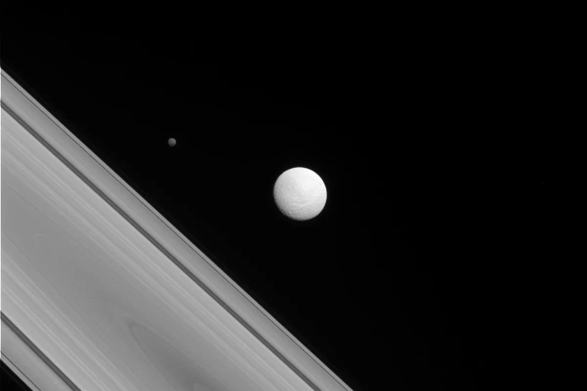 Saturn's bright round moon Tethys beside the diagonal edge of Saturn's rings, with the small dark moon Hyperion to the upper left