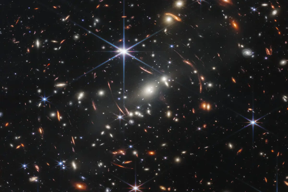 Thousands of galaxies of many shapes and colors on a black background, with bright stars showing six-pointed diffraction spikes, around the galaxy cluster SMACS 0723